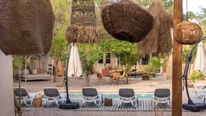 Un área junto a la piscina con sillas de descanso, una piscina pequeña y cestas colgantes de tejido.