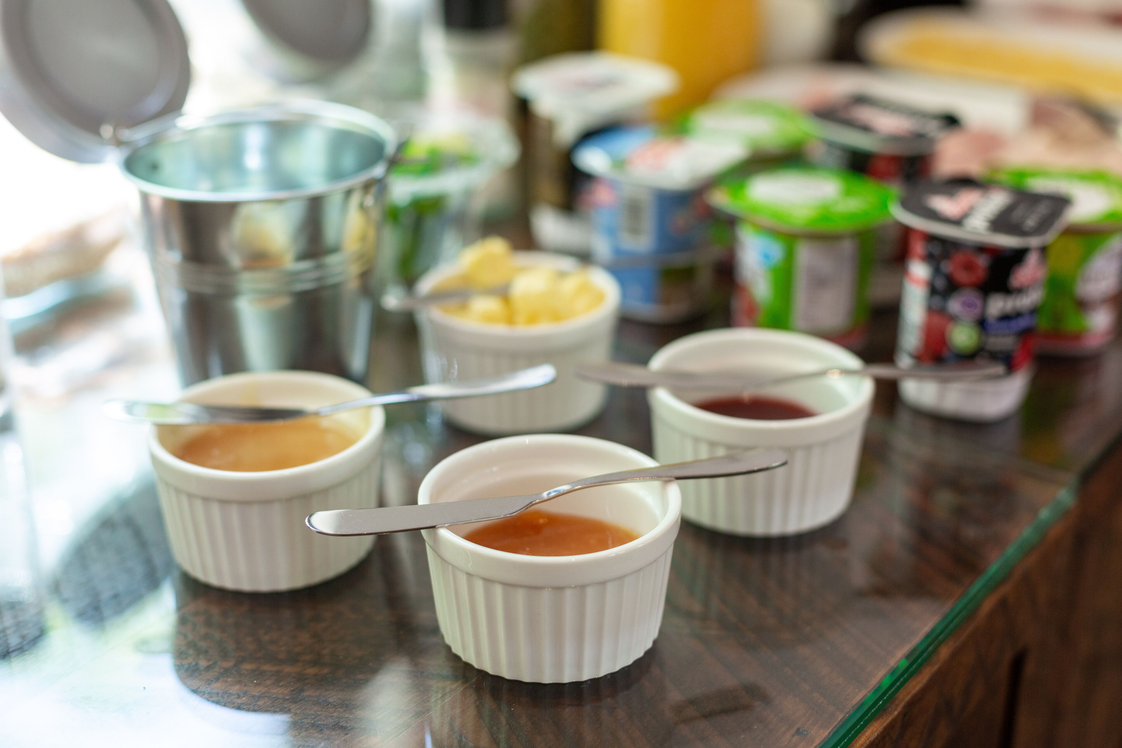 A table with small white ramekins containing various sauces and condiments, accompanied by spoons.