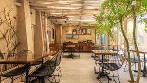 Una cafetería con mesas y sillas de madera, una zona de bar y cuadros en la pared.