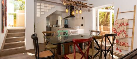 A dining area with a glass table and chairs, a hanging light fixture, and a staircase leading to another room.