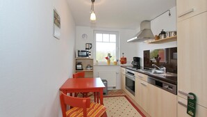 Cocina compacta con mesa y sillas, microondas, estufa y una lámpara colgante.