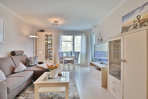 A modern living room with a sofa, coffee table, and TV. There is a dining area with a table and chairs.