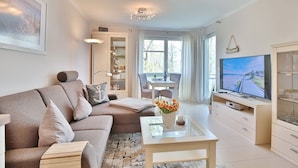 Un salon moderne avec un canapé, une table basse et un téléviseur. On y trouve également un coin repas avec une table et des chaises, ainsi qu’une cuisine équipée de placards et d’un téléviseur.