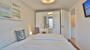 Une chambre à coucher avec un grand lit, une table de chevet, une commode, un miroir et une porte donnant sur une autre pièce.