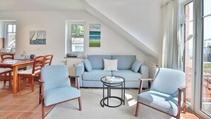 A cozy living room with a blue sofa, two armchairs, a coffee table, and a dining area with a wooden table and chairs.