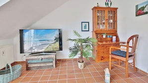 A living room with a television, a wooden cabinet, a chair, a potted plant, and a tiled floor.