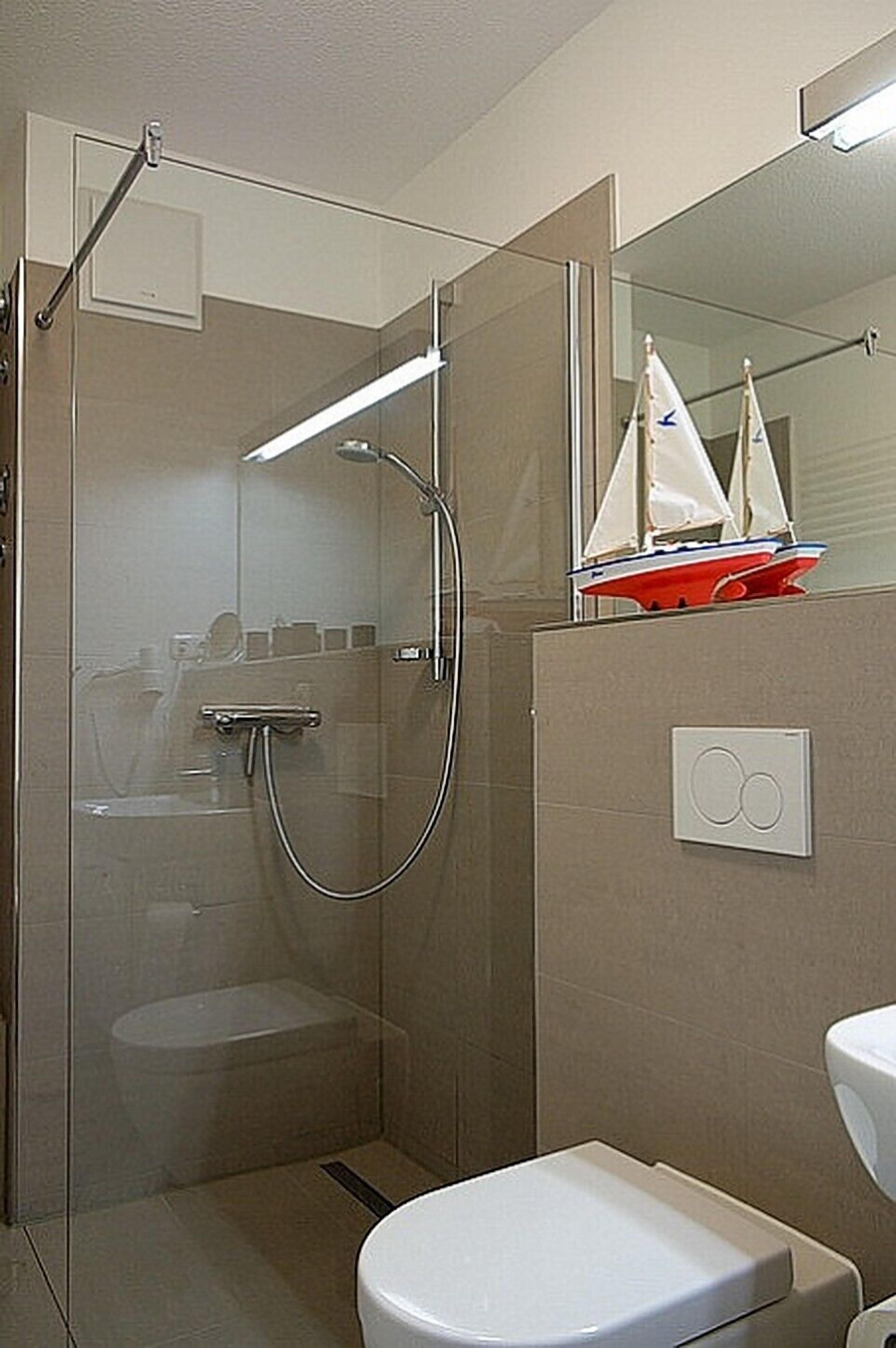 A bathroom with a glass-enclosed shower, a white toilet, and a small sailboat model on the wall.
