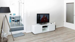 Un soggiorno moderno con una TV a schermo piatto su un mobile bianco, una lampada da terra e un'area pranzo con tavolo e sedie.