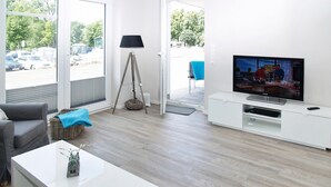 Un soggiorno moderno con televisione, divano, tavolino e lampada.