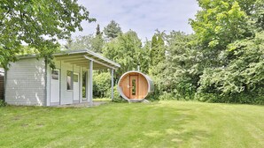 A small, single-story building with a covered porch and a circular wooden structure. - Ferienhaus Ragna Appartement 1 (Haffkrug)