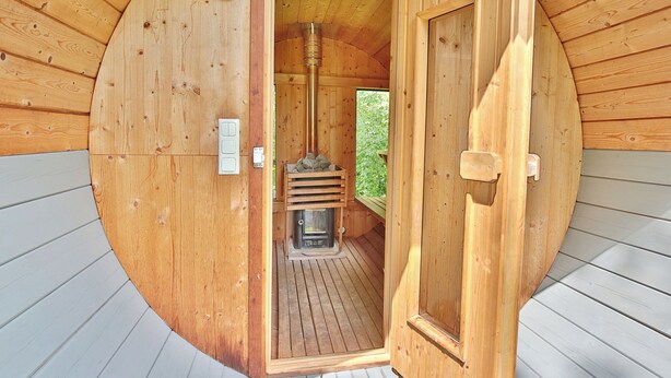 A wooden sauna with a sloped ceiling and a central wood-burning stove. - Ferienhaus Ragna Appartement 1 (Haffkrug)
