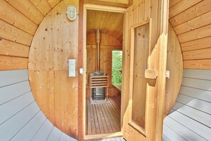 A wooden sauna with a sloped ceiling and a central wood-burning stove. - Ferienhaus Ragna Appartement 2 (Haffkrug)