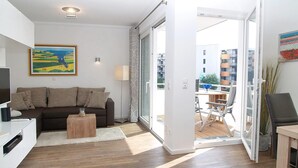 Un saló modern amb un sofà, una taula de centre i una televisió. Hi ha una porta corredissa de vidre que dona a una terrassa exterior.