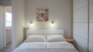 Quarto com cama, mesa de cabeceira, prateleira na parede com objetos decorativos e uma janela.