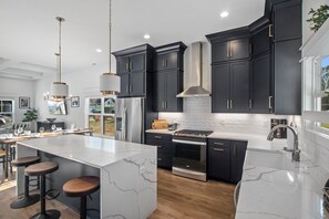 A modern kitchen with dark cabinetry, a large island with stools, stainless steel appliances, and a white marble countertop.