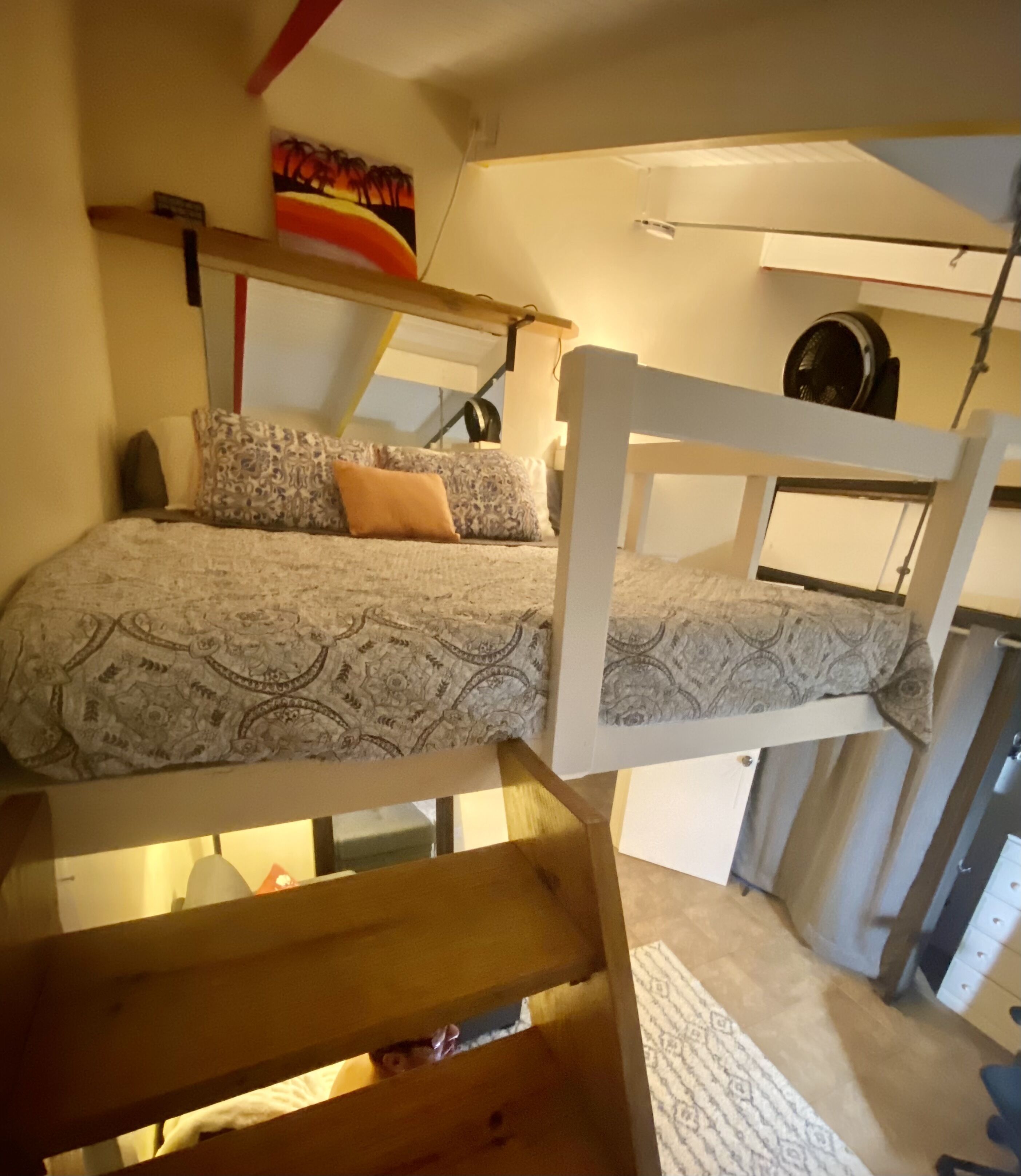 Ein Schlafraum im Schlafsaalstil mit Etagenbetten, einem Schreibtisch und einem Deckenventilator.