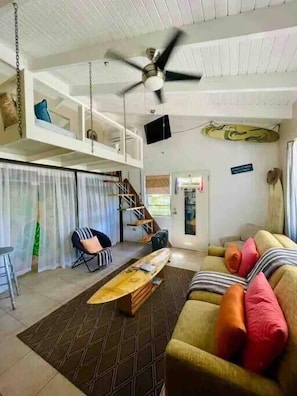 A living room with a ceiling fan, a sofa, a coffee table, and a staircase leading to an upper level. - Vibeinn: 9 Bedroom House w pool-patios (5 King and 4 Queen), Funky Fun 9 Bedroom Rental (East End)
