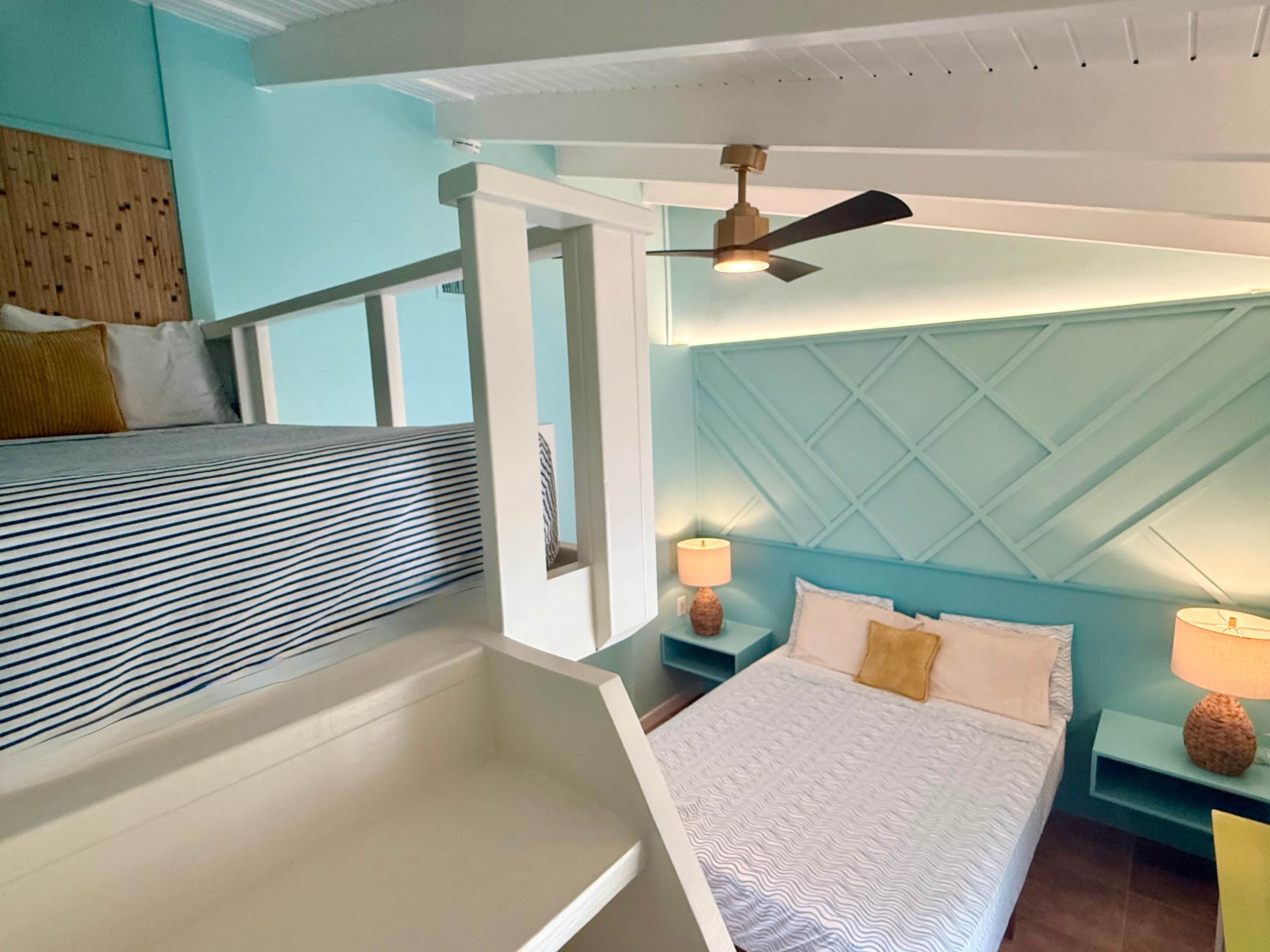 Een kamer met een stapelbed, een enkel bed, een plafondventilator en twee nachtkastjes met lampen.