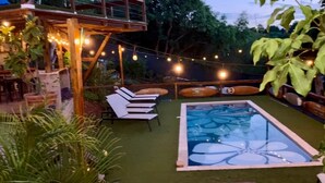 A pool with a floral design, surrounded by lounge chairs and string lights.