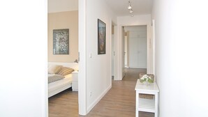 Ein Flur mit einem weißen Sofa, einem kleinen Tisch mit Körben und zwei gerahmten Kunstwerken an den Wänden.