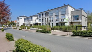 Ein modernes Wohngebäude mit mehreren Balkonen, einer gepflasterten Auffahrt und gepflegter Bepflanzung.
