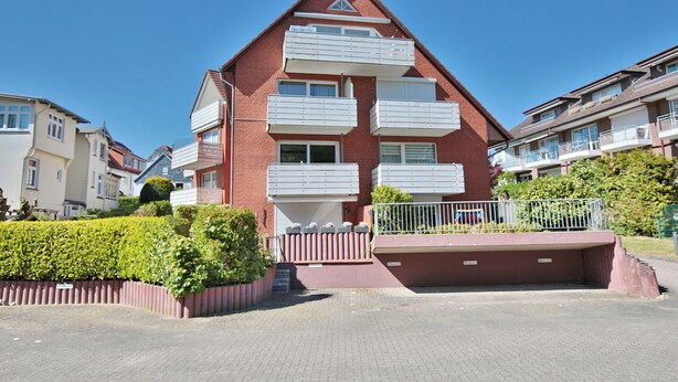 Un edificio residencial de varios pisos con balcones, un camino de entrada pavimentado y un seto bien cuidado.