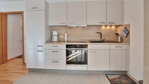 Una cocina compacta con armarios blancos, horno empotrado y cafetera.