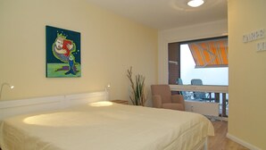 Un dormitorio con una cama grande, un cuadro en la pared, una silla y vistas al balcón exterior.