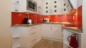 Cocina compacta con armarios blancos, microondas, cafetera y una pared de acento roja.