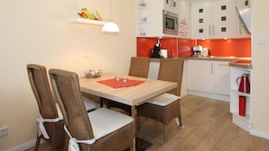 Comedor con mesa de madera y sillas de mimbre, microondas y salpicadero rojo en la cocina.