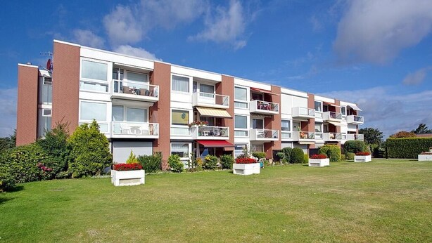 Un edificio residencial de varios pisos con balcones, un toldo rojo y un césped bien cuidado.