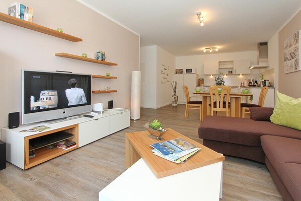 Ein modernes Wohnzimmer mit Flachbildfernseher, Couchtisch aus Holz und braunem Sofa.