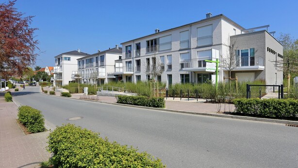 Un immeuble résidentiel moderne doté de nombreux balcons, d’une allée pavée et d’un aménagement paysager bien entretenu.