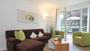 Un salon moderne avec un canapé d’angle marron, un fauteuil vert et une table basse en bois. Un tableau est accroché au mur et une lampe sur pied est posée au sol.