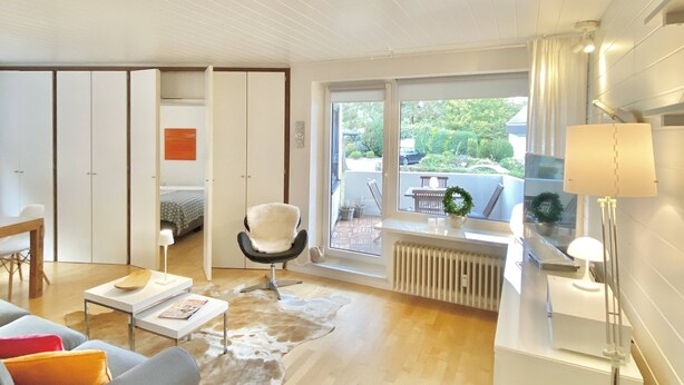 A spacious living room with a large window, a sofa, a chair, a coffee table, and a radiator. - Strand und Meer Appartement 1 (Scharbeutz)