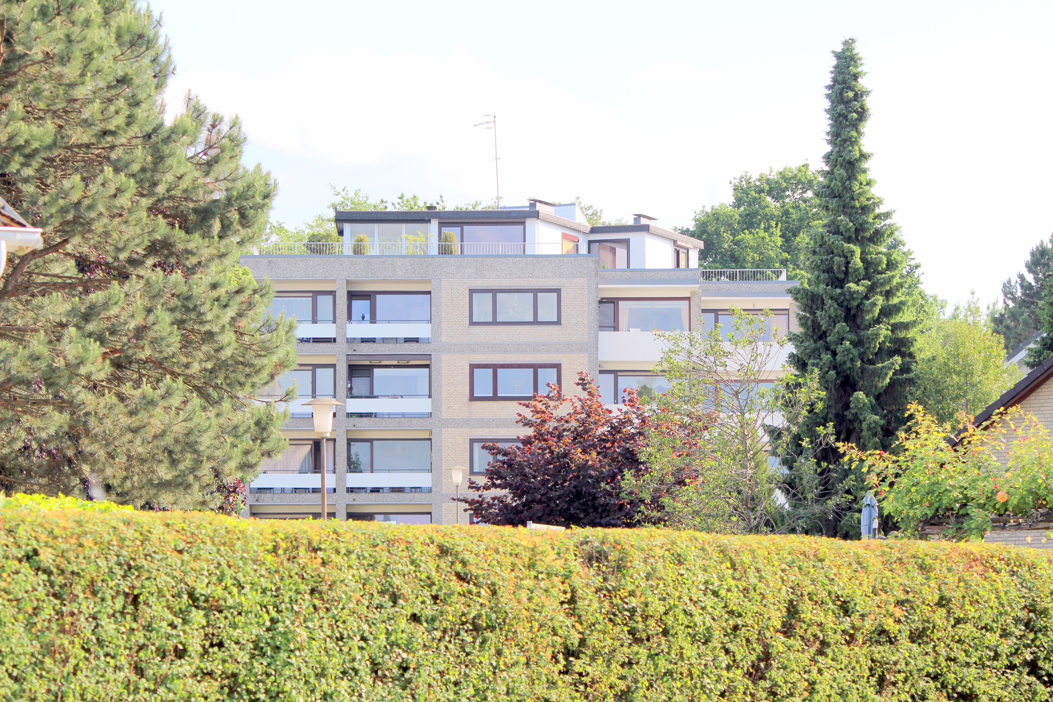 A multi-story residential building with balconies, surrounded by well-maintained hedges and trees.