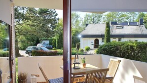 A balcony with a table and chairs, a potted plant, and a view of a house and parked cars. - Strand und Meer Appartement 1 (Scharbeutz)