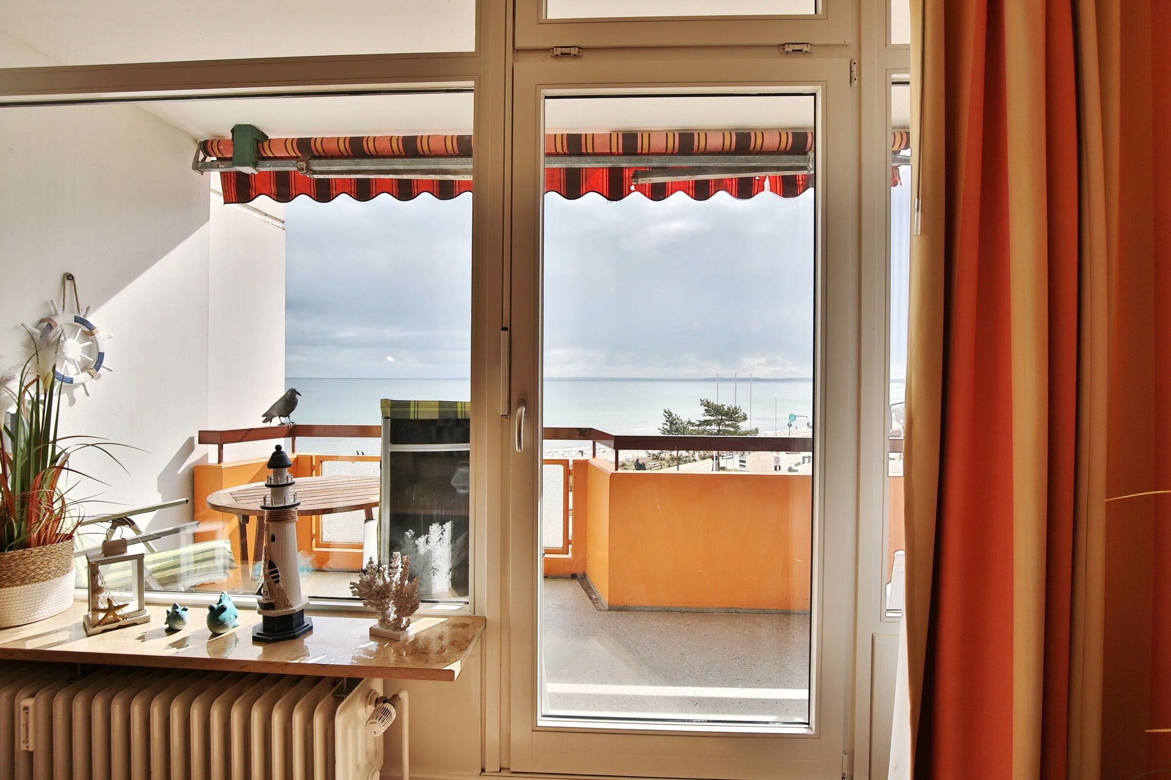 A room with a view of the sea through a glass door, a small table with decorative items, and a potted plant.