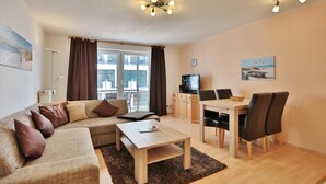 Een moderne woonkamer met een bank, salontafel en eethoek. Er is een televisie, een klok en kunst aan de muren.