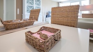 A room with a white table, two wicker baskets, and a wicker chair. - Strandglück Appartement 8A Strandgutfinder.de (Scharbeutz)