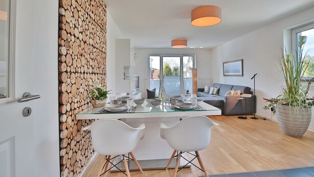 Une cuisine moderne avec un îlot central en verre, des chaises blanches et un mur décoré de rondins de bois.