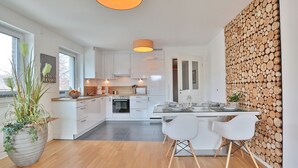 Une cuisine moderne avec des meubles blancs, une table à manger en bois et deux chaises blanches.