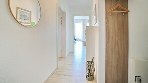 A hallway with a wooden floor, a round mirror, and a wooden door. - Parkblick Appartement 4 (Scharbeutz)