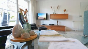 A modern office with a glass table displaying decorative items, a wooden sideboard, a television, and a view of the outdoors. - Parkblick Appartement 4 (Scharbeutz)