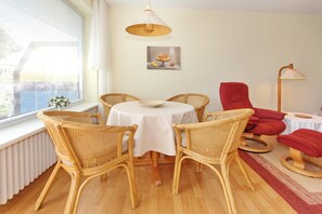 Ein Essbereich mit Korbstühlen, einem runden Tisch, einem roten Sessel, einer Stehlampe und einem Gemälde an der Wand.