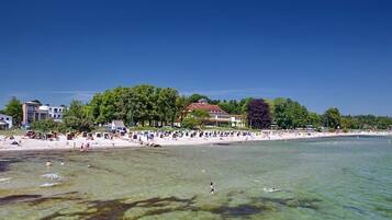 A beach with clear water, people swimming, and buildings in the background.