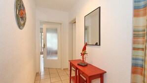 A hallway with a tiled floor, a red table with a bird sculpture, a mirror, and a door leading to another room.