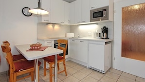 A compact kitchen with white cabinets, a microwave, a coffee maker, and a dining area with a table and chairs.