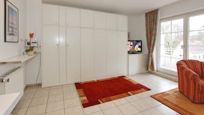 A living room with a large white wardrobe, a red rug, a striped sofa, and a television on a stand.