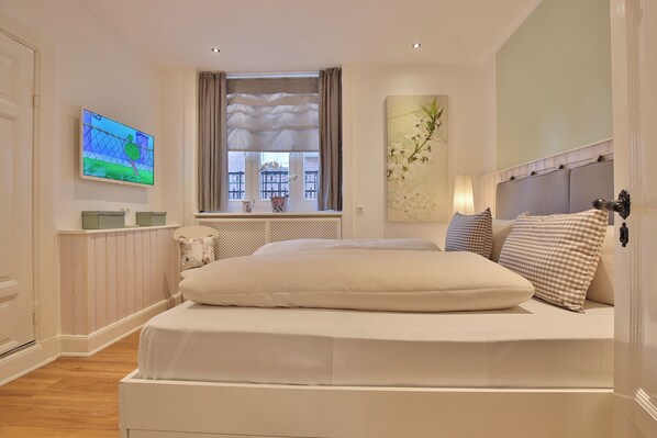 Un dormitorio con una cama grande, un televisor en la pared, una ventana con cortinas y un adorno decorativo en la pared.